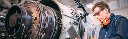Aircraft engineer in a hangar using a laptop while repairing and maintaining an airplane jet engine