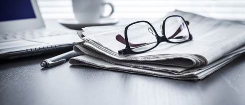 Table with laptop, coffee, pen, newspaper and glasses